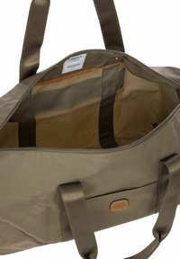 Khaki nylon reistas met dubbele stoffen handvatten, ritssluiting en een ruime binnenkant met een gladde beige voering en label.