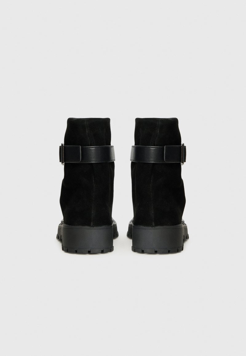 Schwarze Wildleder-Stiefeletten mit strukturiertem Finish, versehen mit einem schwarzen Lederband und Schnallen-Detail sowie einer robusten Gummisohle.