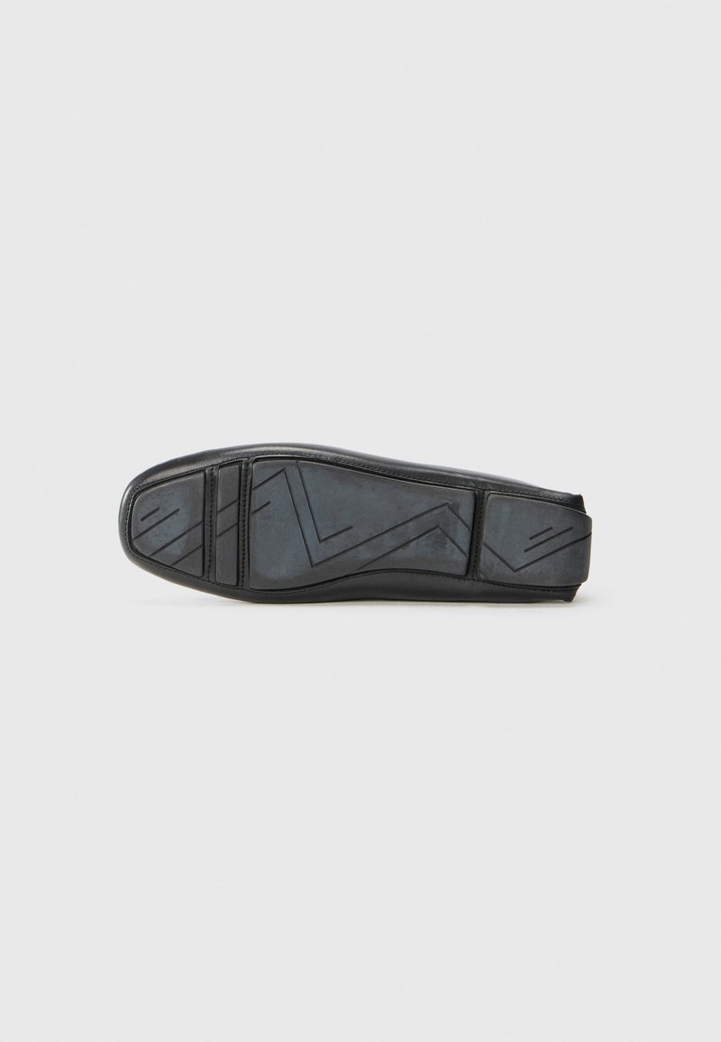 Scarpa nera piatta con tomaia liscia, suola in gomma con pratiche trame geometriche e un design elegante.