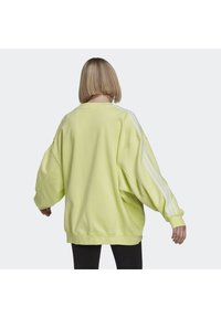 Přepychová mikina ve neonově žluté barvě s měkkou texturou, která má bílý design se třemi pruhy na rukávech a žebrované manžety.