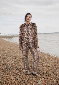 Barna és bézs tónusú, gombos záródású leopárdmintás műszőrme kabát, hozzáillő, leopárdmintás, szárában bővülő nadrággal párosítva.