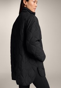 Zwarte gewatteerde overshirt met een hoge kraag, voorzien van een relaxed fit en een ronde zoom, gemaakt van lichtgewicht stof met zichtbare stiksels.