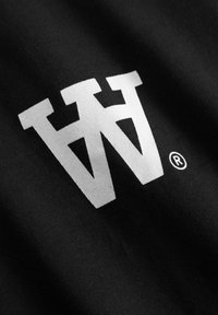 Hvide "AW" bogstaver og et registreret varemærkesymbol trykt på sort stof, der viser tekstur og lette folder.