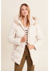 Giacca bianca voluminosa con cappuccio foderato in finta pelliccia, motivo a rombi, zip frontale e tasche laterali. Modella con pantaloni verde oliva.