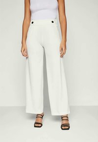 White wide-leg pants made of smooth fabric, featuring a high waist, large side pockets, and black button accents. Paired with a fitted white top.
