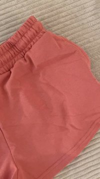 Pantaloni scurți de corai deschis, dintr-un material moale, având un tiv elastic și un design simplu, fără modele sau elemente din metal vizibile.