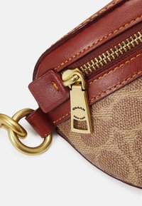 Borsa in tessuto marrone con motivo monogram, caratterizzata da dettagli in pelle rossa, ferramenta dorata e cerniera con tiretto brandizzato. Dettaglio anello circolare dorato.