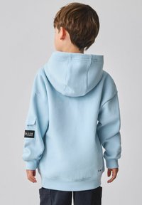 Hele sinine kapuutsiga dressipluus, mis on valmistatud pehmest kangast, mahuka kapuutsi ja avarate varrukatega ning vasakul käel on bränditud silt.