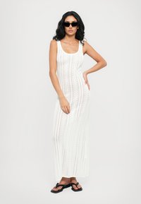 White, knitted maxi dress with vertical stripes, scoop neckline, and fitted silhouette. Paired with black flip-flops and sunglasses.