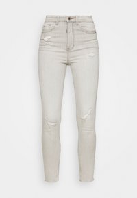 Vaqueros de tiro alto en gris claro con un ajuste slim, que cuentan con detalles de desgaste en las rodillas, diseño clásico de cinco bolsillos y un cierre de botones.