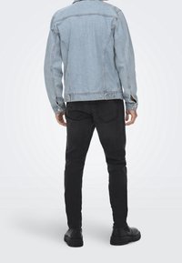 Ljust blå denimjacka med långa ärmar, bakömmar och silverdetaljer, kombinerad med svarta jeans och svarta skor.