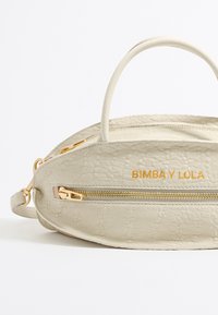 Piccola borsa in pelle crema con finitura testurizzata, dotata di manico superiore, hardware dorato e tasca frontale con zip. "BIMBA Y LOLA" impresso in oro.