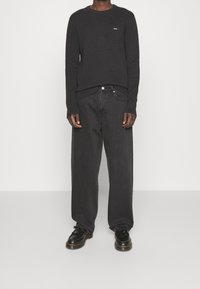 Černý žebrovaný pletený svetr s dlouhými rukávy s malým logem, kombinovaný s volnějšími tmavě šedými denimovými džíny a černými šněrovacími botami.