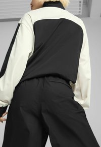 Black and cream jacket with a high collar, featuring a contrasting back panel. Designed with a relaxed fit and elastic waistband.