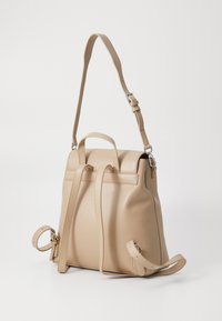 Beige lær ryggsekk med justerbare stropper, topphåndtak og jevn tekstur. Har et minimalistisk design og sølvfargede detaljer.