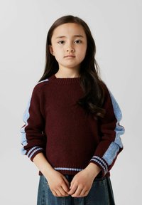 Burgundy tröja med blå ärmar, ribbad halsringning och randiga detaljer vid ärmsluten. Mjuk textur och avslappnad passform. Bärs med en denimkjol.