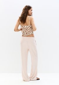 Blusentop mit Blumenmuster und verstellbaren Trägern, kombiniert mit lockeren, hellrosa weit geschnittenen Hosen. Weiche Textur und entspannte Silhouette.