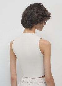 Top smanicato aderente in tessuto beige chiaro con texture liscia, caratterizzato da un collo alto e un design corto.