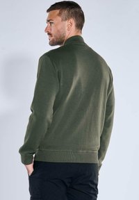 Dark green sweatshirt with a ribbed collar and cuffs, featuring a soft textured fabric and a simple, casual design. Simple stitching details.