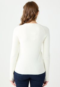 Pull blanc à côtes avec des manches longues et un col rond, présentant un design ajusté et des détails de couture subtils le long des coutures.