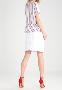 Gestreepte blouse met korte mouwen in wit, rood en blauw, gecombineerd met een strakke witte rok. Bevat rode hoge hakken met enkelbandjes.