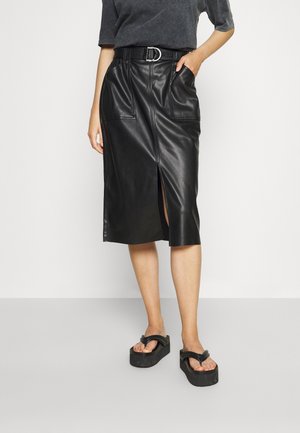 Musta nahkainen midihame sivuhalkiolla, etutaskuilla ja vyötäröltä kiristettävä. Yhdistetty paksupohjaisiin mustiin varvassandaaleihin.