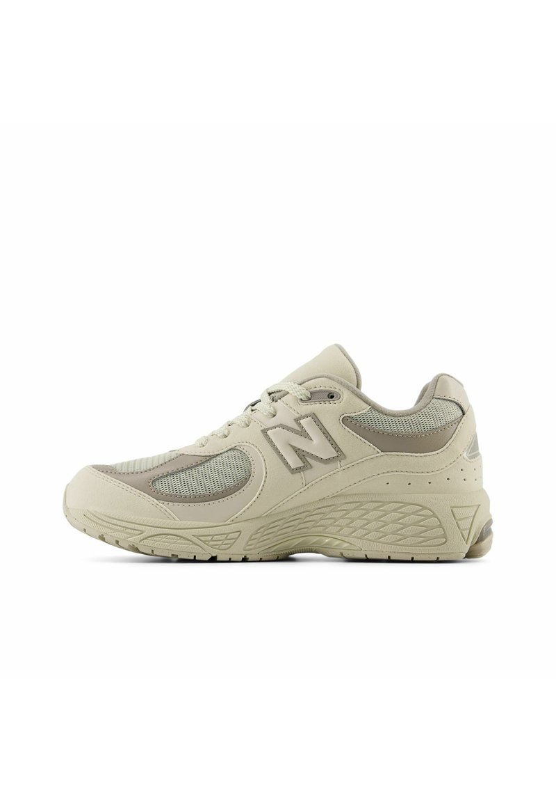 Scarpa sportiva beige con pannelli in rete, suola in gomma, intersuola imbottita e logo "N" sul lato, caratterizzata da una punta arrotondata e dettagli testurizzati.