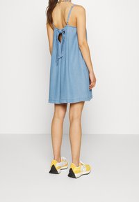 Jeanskl�änning med justerbara spagettiställ och knyt bak. Har en avslappnad passform och knälång nederkant. Bärs med gula sneakers.