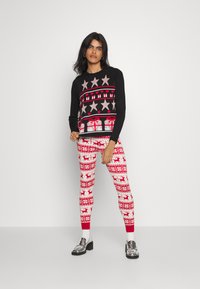 Black sweater with silver stars and red heart patterns, paired with red and white leggings featuring reindeer and geometric designs. Silver shoes.