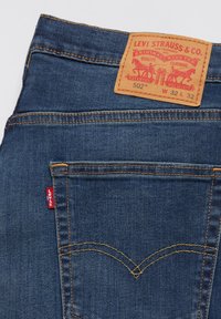 Dunkelblaue Denim-Jeans mit orangefarbenen Nähten, ausgestattet mit einem Lederlabel an der Taille und einem kleinen roten Tab an der Gesäßtasche.