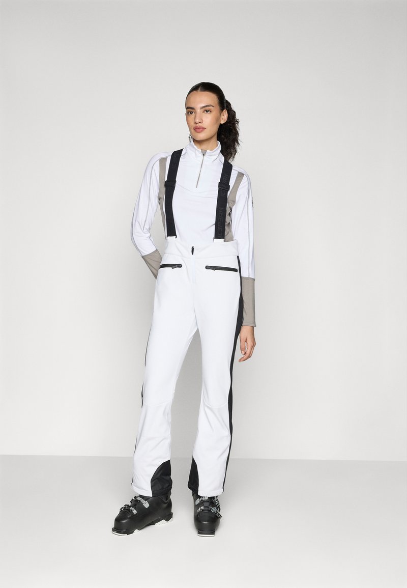 Overoles de esquí blancos con tirantes ajustables negros, dos bolsillos con cremallera y paneles laterales en negro contrastante, combinados con una parte superior de color gris claro.