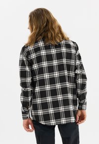 Zwart-wit geruit flanellen overhemd met lange mouwen en een button-down kraag, met een gebogen onderkant en zijsplitten voor een comfortabele pasvorm.