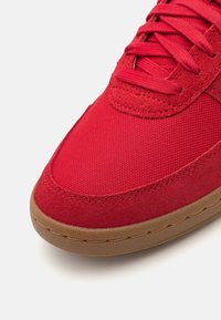 Röda textilsneakers med en slät mockahuvudkappa, texturerad nätkropp, platta snören och en hållbar sula av gummibel�äggning.