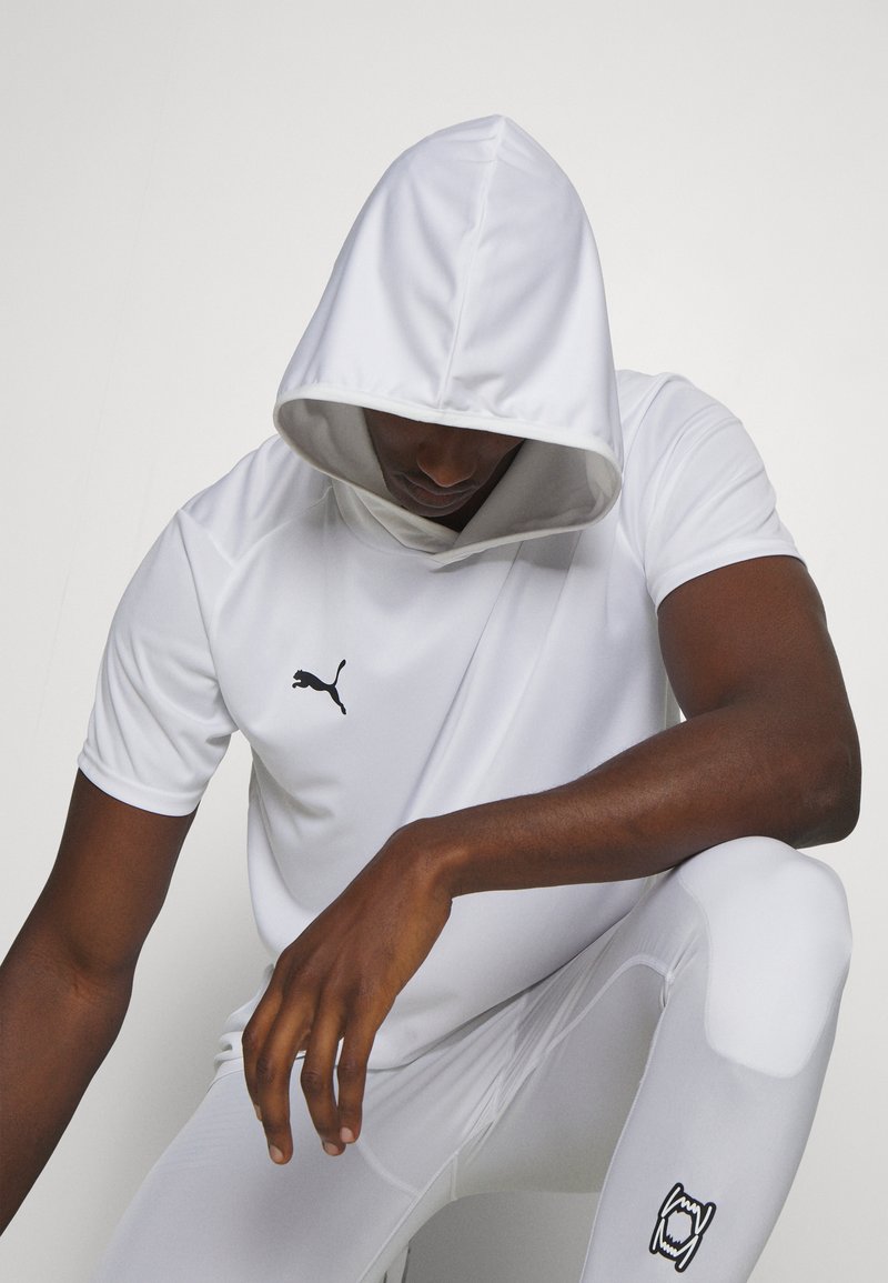 Felpa corta bianca con maniche corte e un ampio cappuccio, con un grande logo Puma nero sul lato sinistro del petto. Tessuto opaco e liscio con uno stile atletico aderente.