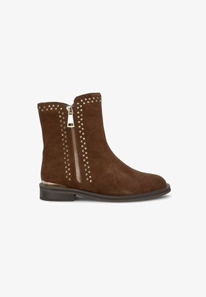 Bruine suède enkellaarzen met een zijrits met zilverkleurige hardware en studs langs de bovenkant en ritssluiting.