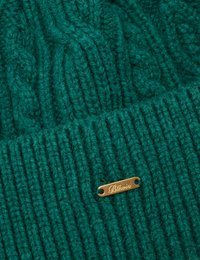 Groene gebreide muts met kabel- en ribbelpatronen. Bevat een klein gouden label met gegraveerde tekst. Gemaakt van dik garen voor warmte.