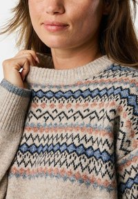 Strickpullover mit einem gerippten Halsausschnitt, ausgestattet mit einem geometrischen Muster in Blau-, Schwarz-, Pfirsich- und Grautönen auf einem hellbeigen Hintergrund.