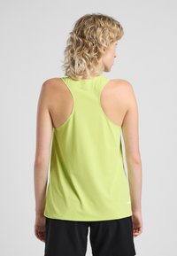 Lichtgroene sportieve tanktop met een gestructureerde stof, racerback ontwerp en een afgeronde zoom, gedragen met zwarte shorts. Geen zichtbare merken.