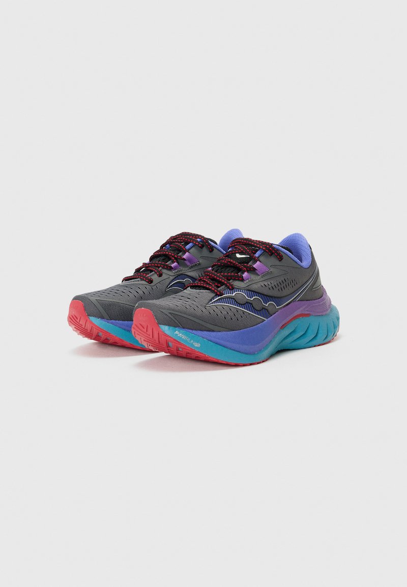 Zapatillas deportivas grises con acentos morados y cordones rojos. Suela gruesa y texturizada con una franja azul. Material superior transpirable con un diseño patrimonial.