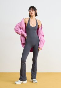 Mono gris con escote halter y piernas acampanadas, superpuesto con una camisa de pana rosa de gran tamaño, combinado con zapatillas multicolor.