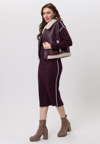 Bordeauxrode leren jas met een schapenvachtkraag, gecombineerd met een bijpassende strakke jurk met een witte zijstreep. Bruine enkellaarsjes met hak.