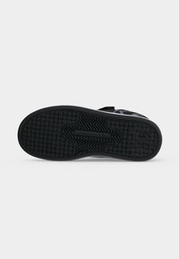 Semelle de sneaker noire avec motifs de grip texturés incluant des carrés et des zigzags, logo de marque visible sur la zone du talon.