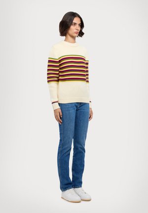Maglione crema con righe orizzontali multicolori, abbinato a jeans blu e sneakers bianche. Il maglione ha un collo rotondo e polsini a coste.