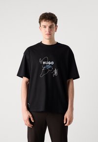 Black cotton t-shirt with short sleeves, featuring blue and white embroidered “HUGO” logo and creative graphics on the chest.