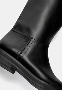 Stivale nero in pelle fino al ginocchio con una finitura liscia, caratterizzato da cuciture orizzontali lungo il gambale e una suola in gomma piatta.