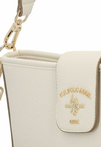 Vit läderhandväska med små korn och ett guldemblem. Har en klaffstängning och guldfärgade metalldetaljer med en strukturerad form.