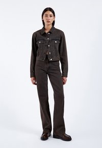 Dunkelblaue Jeansjacke mit spitzem Kragen, Fronttaschen und silbernen Knöpfen, kombiniert mit passenden hoch taillierten, ausgestellten Hosen und schwarzen Stiefeln.