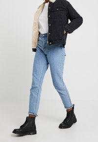 Svart denimjacka med konstigt fårfoder, vit t-shirt, ljusblå högmidjade jeans och svarta snörstövlar.