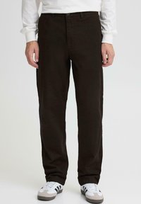 Pantalones marrones de corte recto hechos de algodón, con cierre de botón y bolsillos laterales, combinados con zapatillas blancas con detalles en negro.