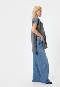 Top grigio a maniche corte realizzato in un tessuto morbido, abbinato a jeans blu a vita alta e a gamba larga con una vestibilità rilassata e tasche laterali.